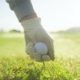 Golfer steckt Tee mit Golfball in den Rasen