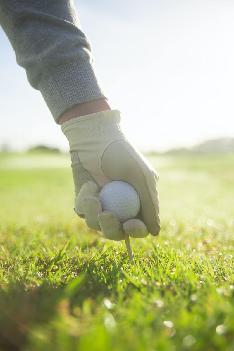 Golfer steckt Tee mit Golfball in den Rasen